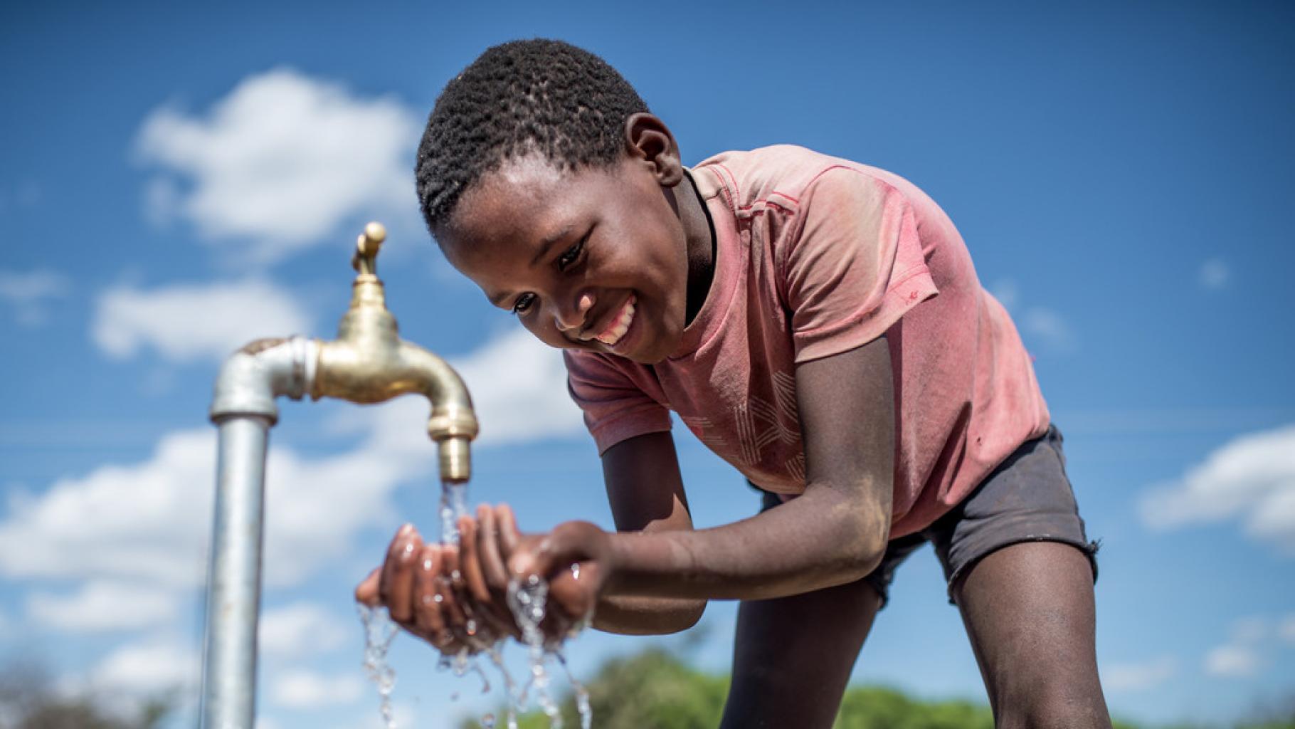 Ein Kind fängt Wasser aus einem Wasserhahn mit den Händen auf.