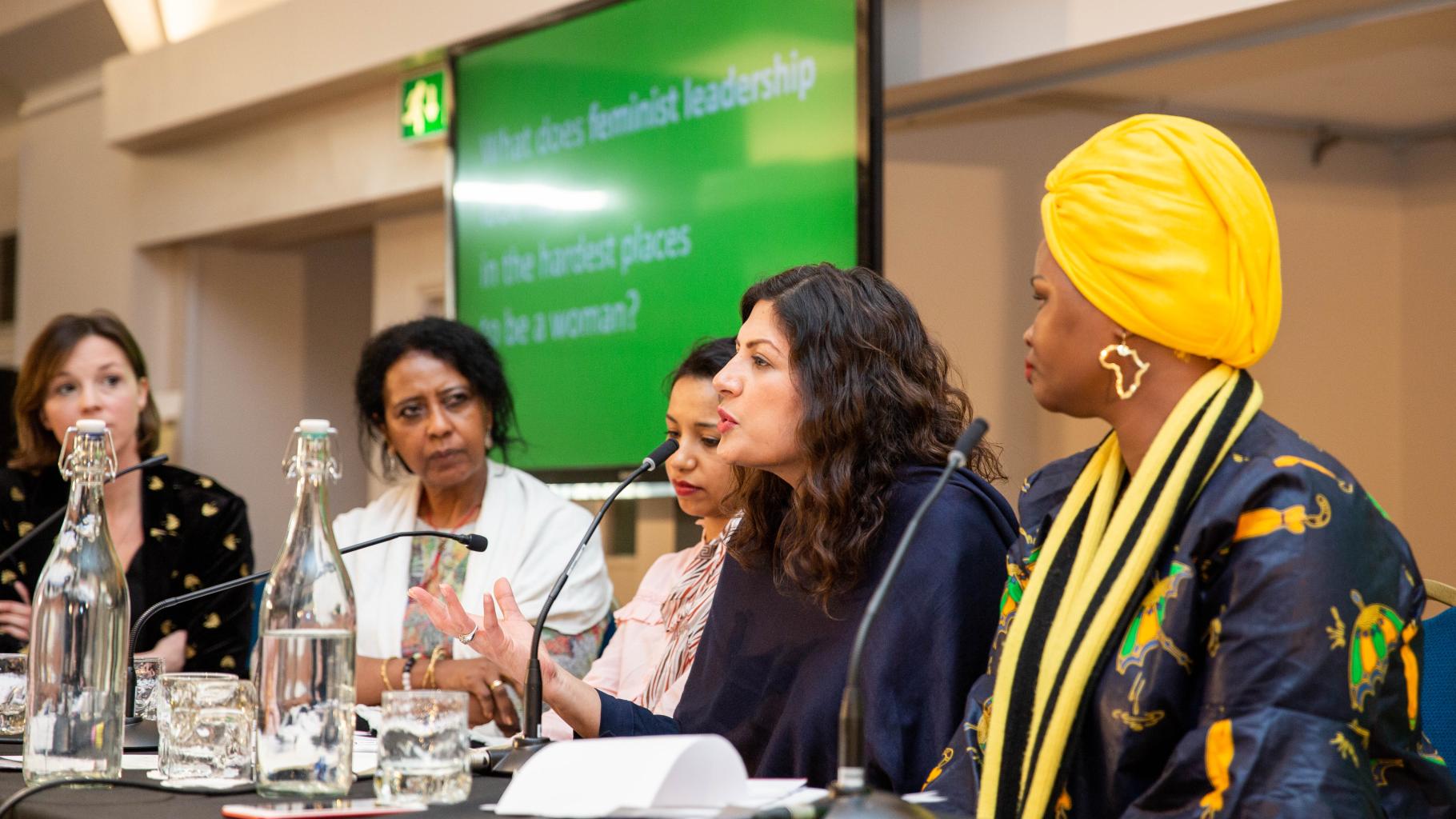 Annie Kelly, Hala Al Karib, Rasha Obaid, Preet Kaur Gill MP und Riya William Yuyada sitzen an einem Tisch mit Tischmikrophonen und tauschen sich vor einem Publikum aus