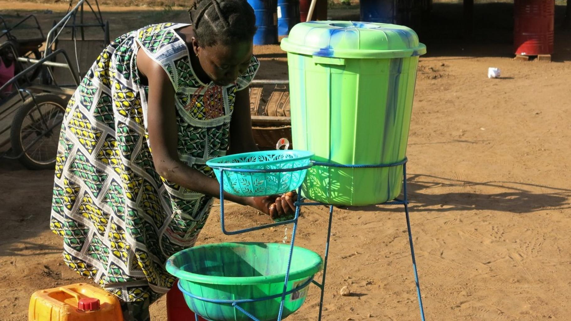 Priscilla Bisset beugt sich zum Händewaschen zum einem grünen Eimer. Neben ihr steht ein gelber Wasserkanister.