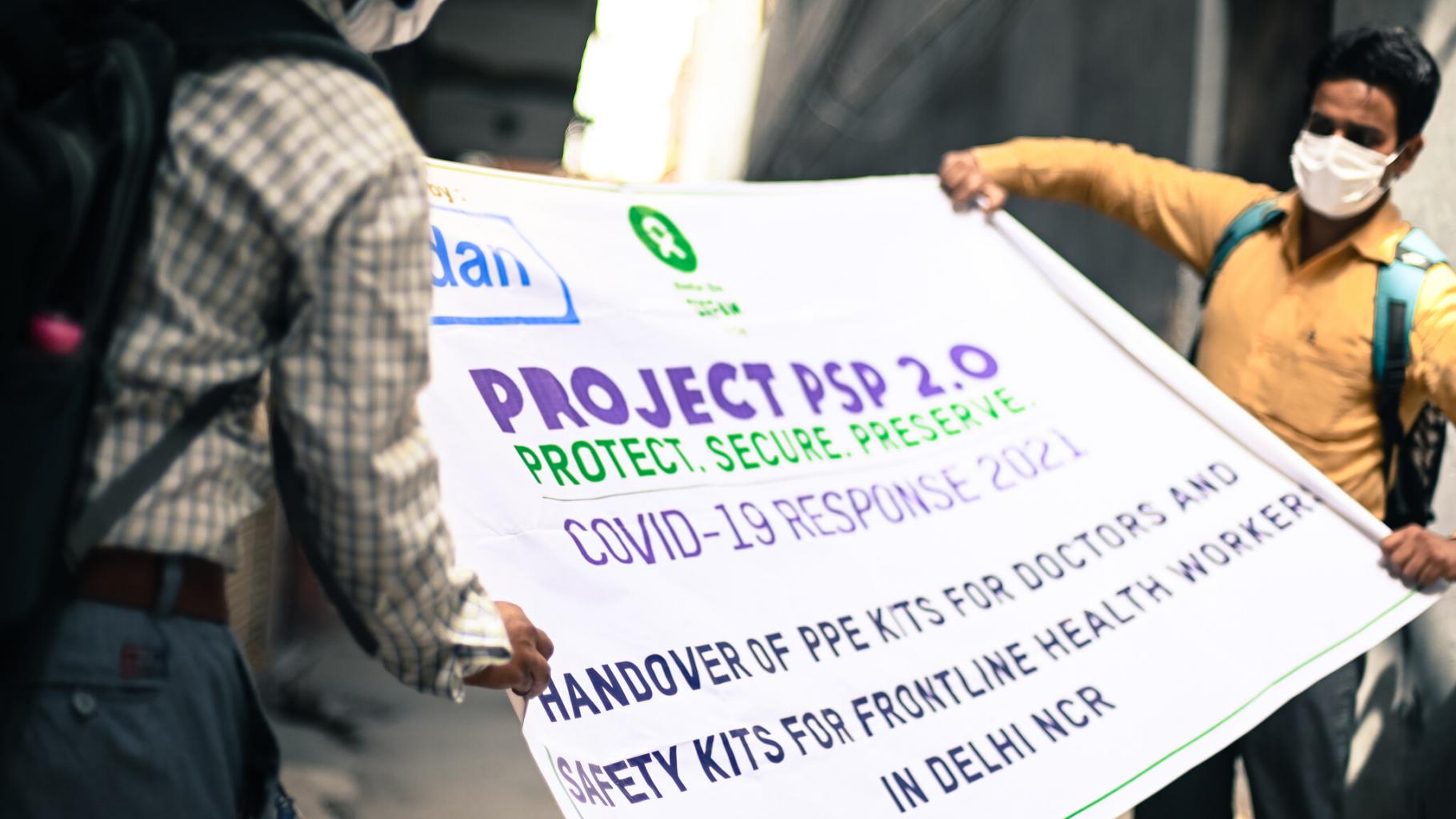 Zwei Arbeiter verpacken ein Werbeplakat, das auf die Verteilung von persönlicher Schutzausrüstung für medizinisches Personal in Neu-Delhi aufmerksam macht