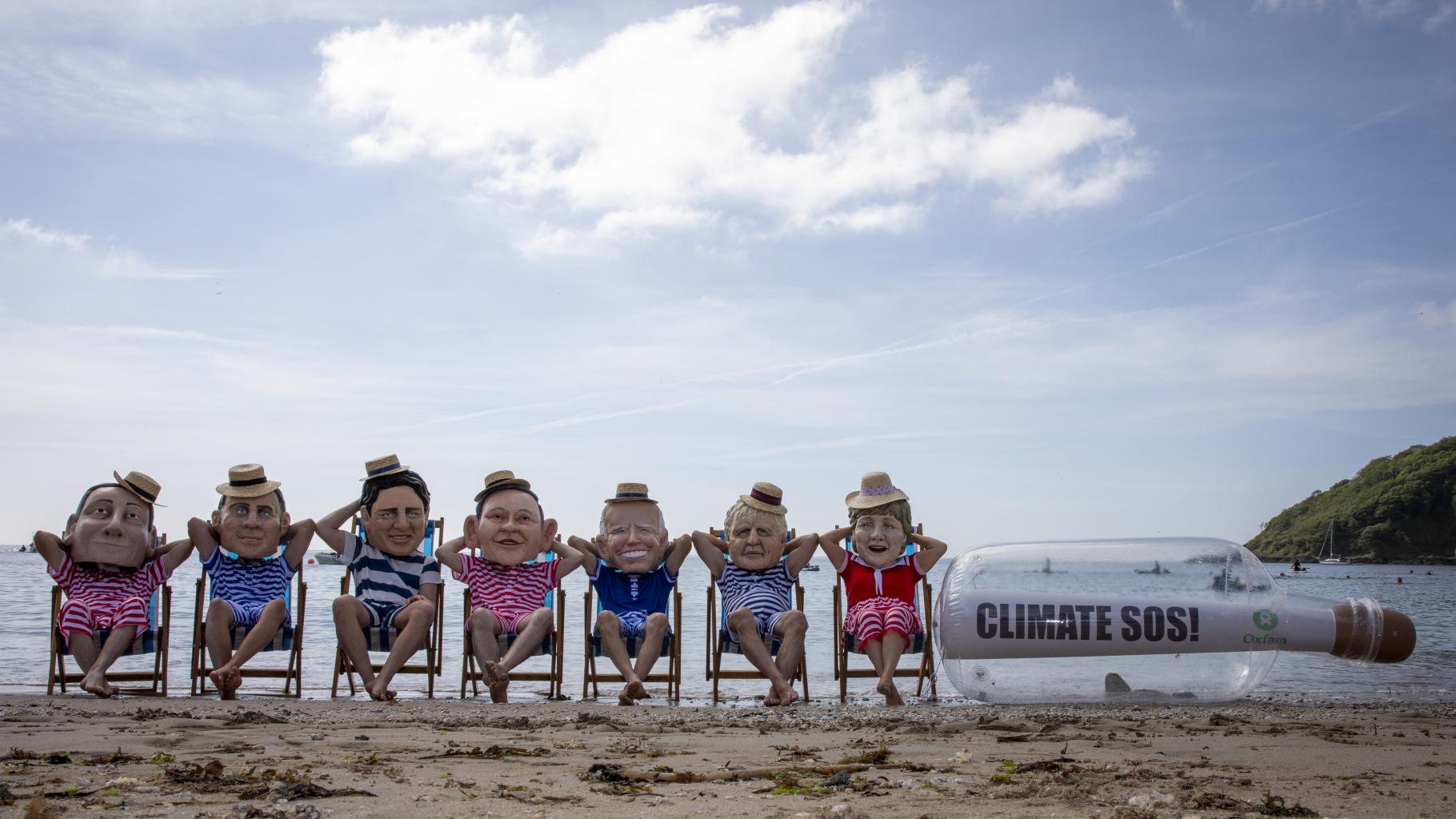 Aktivist*innen posieren als G7-Regierungschef*innen am Strand. Sie tragen gestreifte Badesachen und Sonnenhüte.