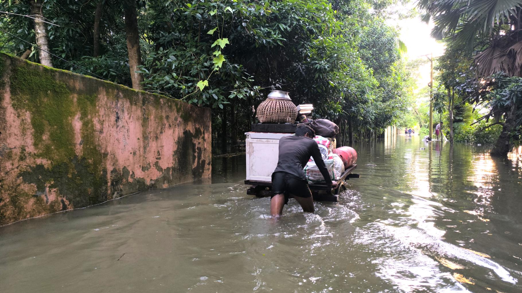 Ein Mensch schiebt sein Hab und Gut auf einem Wagen durch knietiefes Wasser