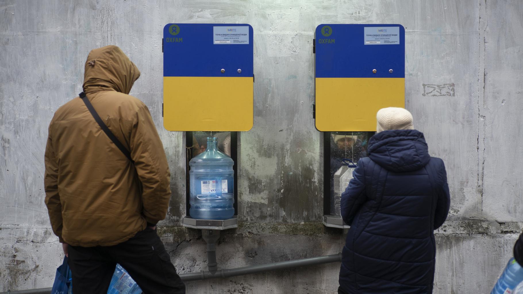 Zwei Personen holen Wasser an einer Wasserstelle von Oxfam. In der Stadt Mykolaiv wird Trinkwasser bereitgestellt, weil die Wasserleitungen in den Häusern zerstört wurden.