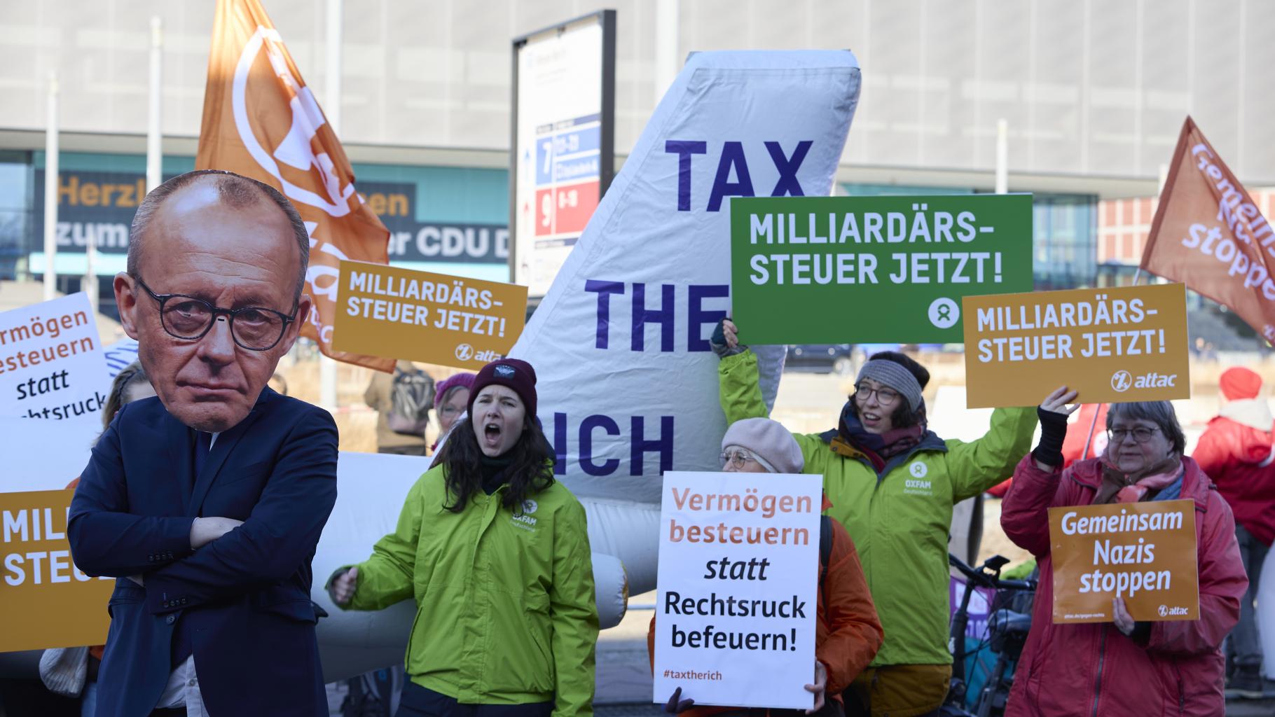 Eine Gruppe von Menschen steht auf der Straße und hält Schilder hoch. Darauf fordern Sie eine Milliardärssteuer von Friedrich Merz.