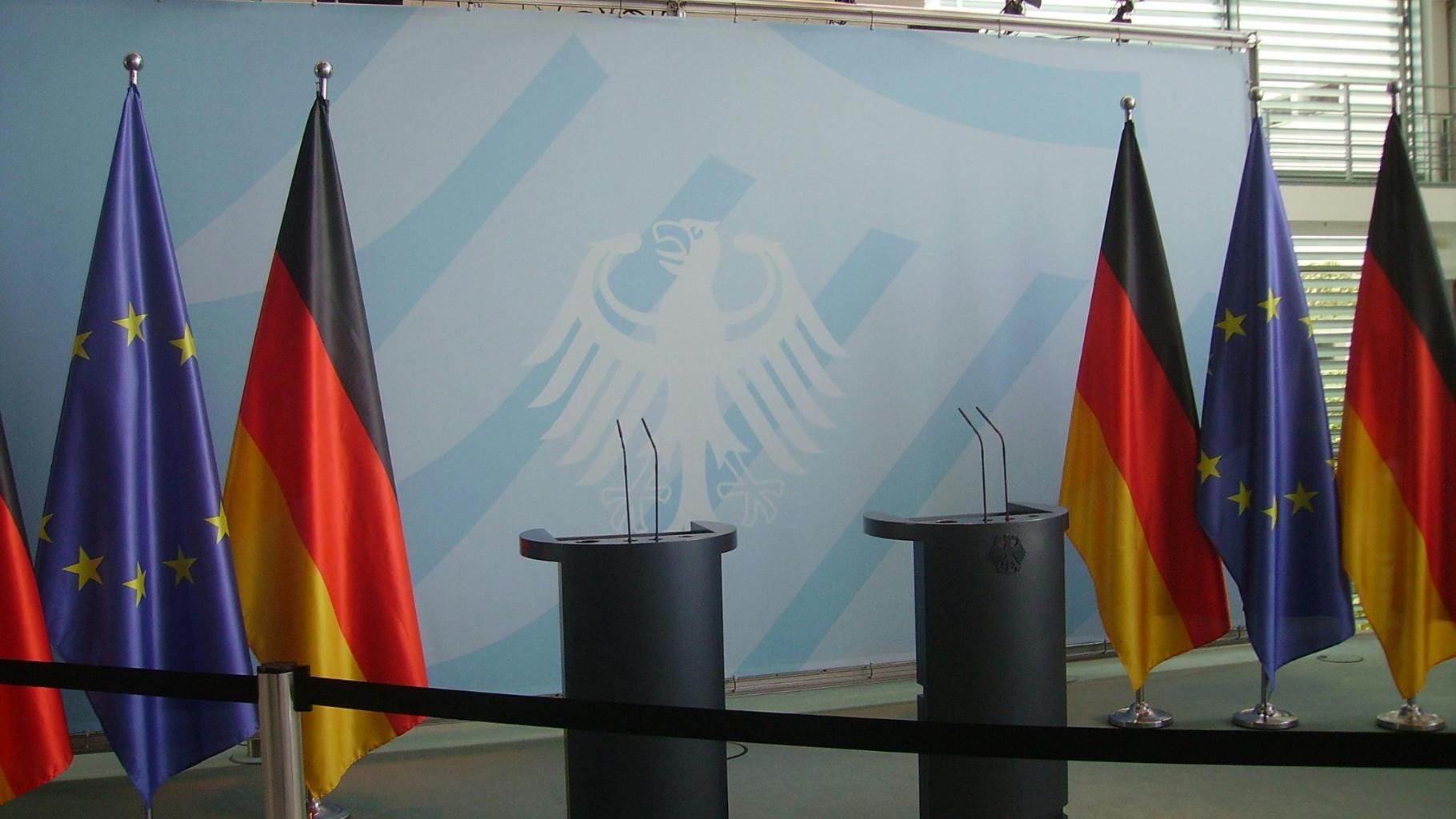 Flaggen der Europäischen Union und der Bundesrepublik Deutschland hängen neben zwei mikrofonierten Redepulten