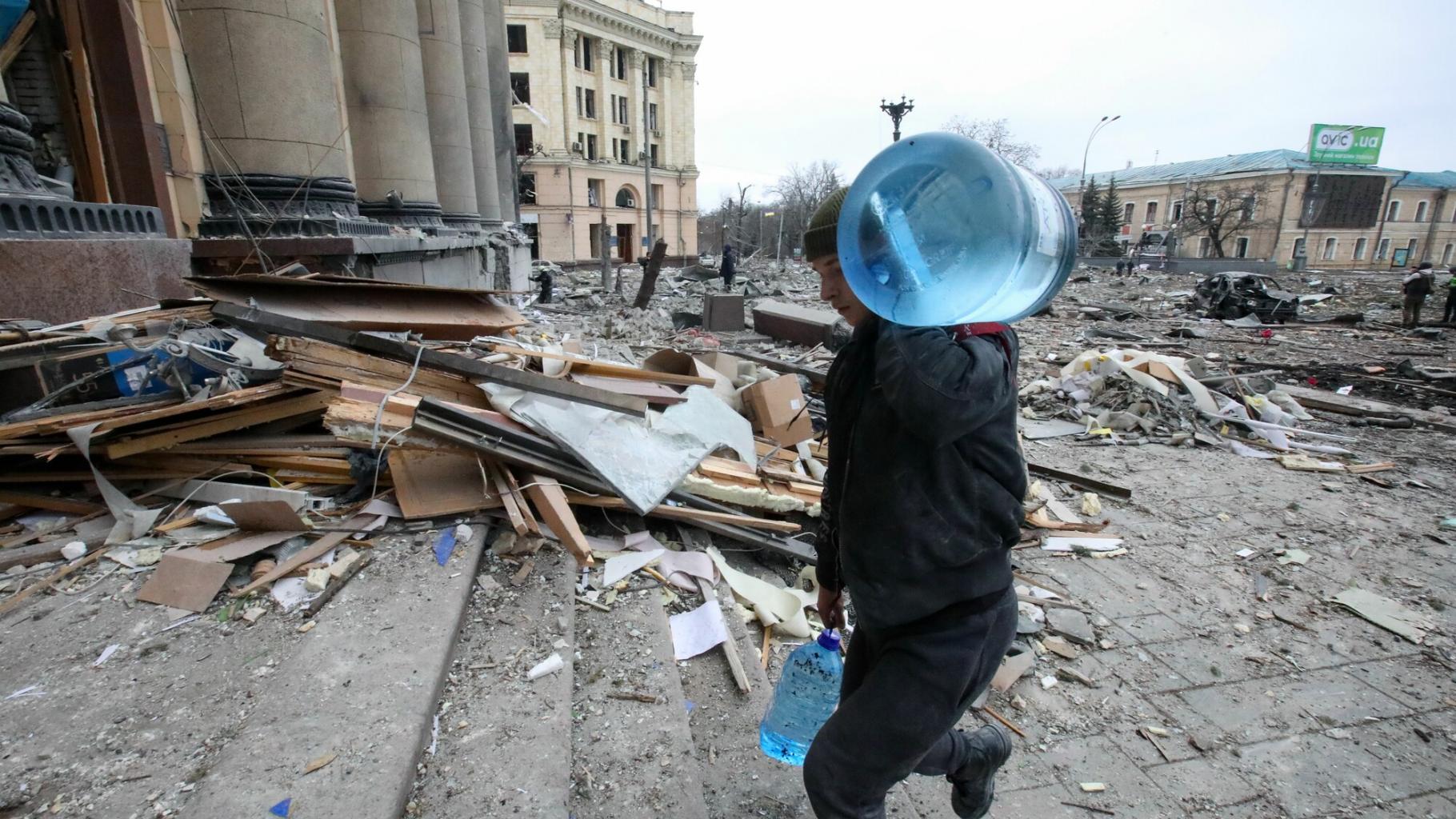 Ein Mann trägt Wasserbehälter in das beschädigte Gebäude der staatlichen Regionalverwaltung von Charkiw, Ukraine