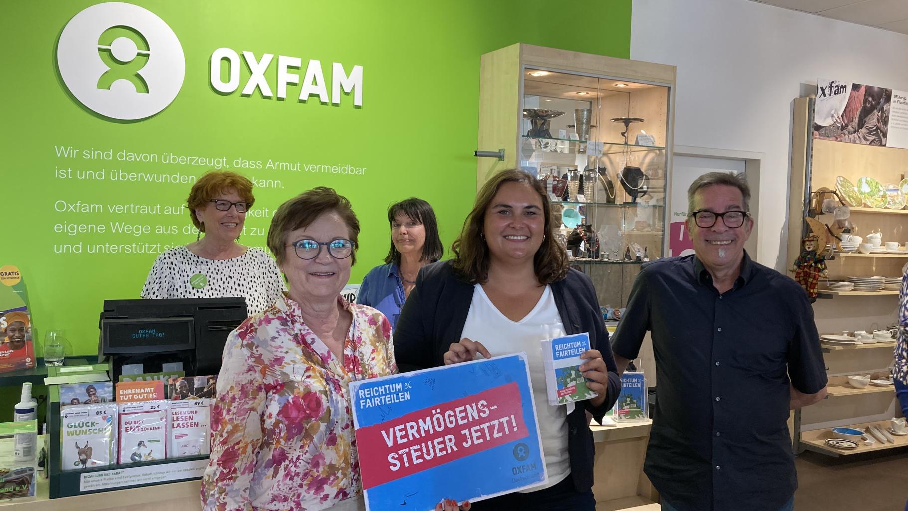 In einem Oxfam Shop übergeben Menschen Postkarten mit der Aufschrift „Reichtum fairteilen – Vermögenssteuer jetzt!“ an die Isabel Cademartori