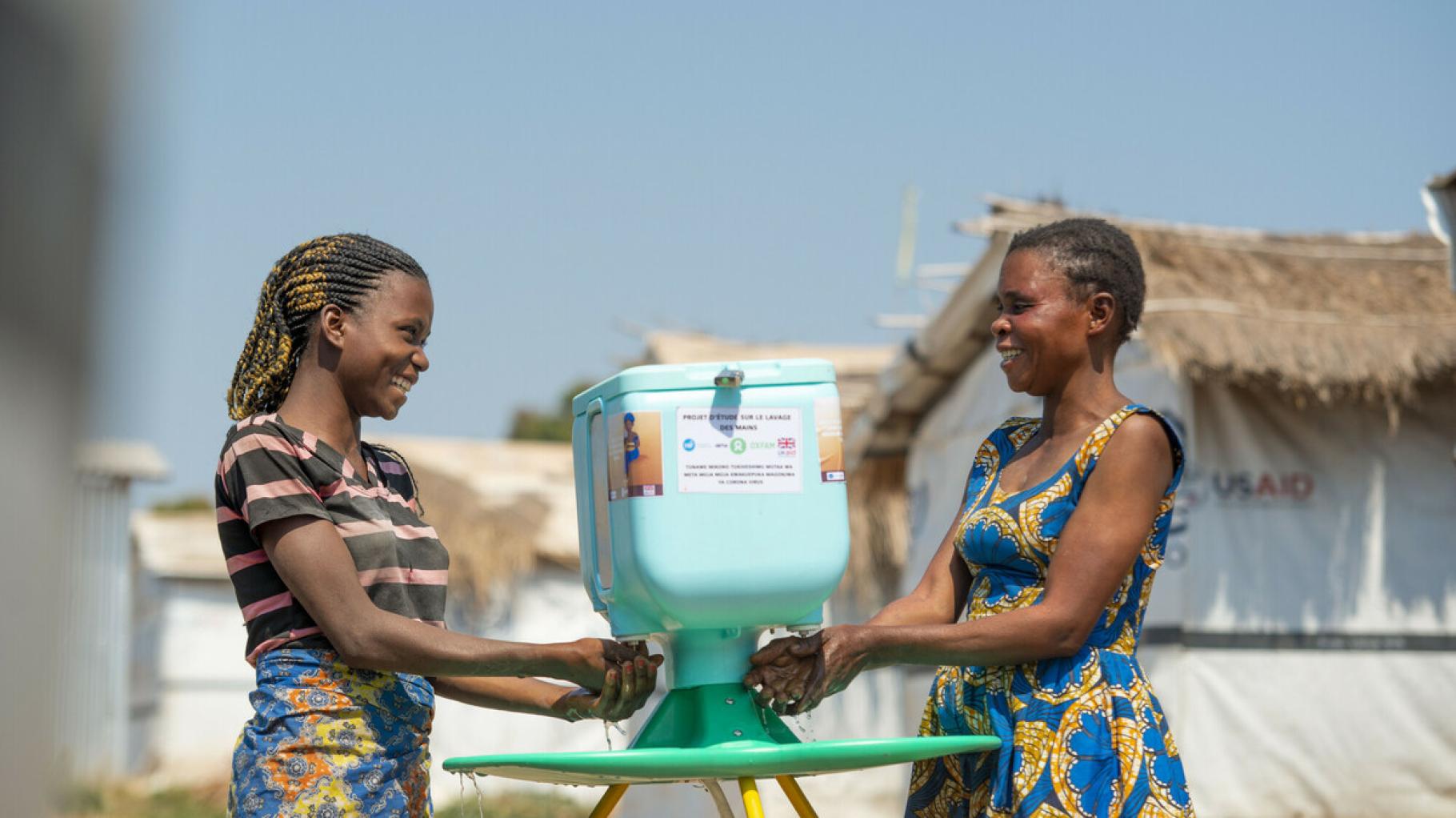 Zwei Frauen waschen ihre Hände an einer Handwasch-Station im Geflüchtetencamp in Kisalaba (Demokratische Republik Kongo). Die Frauen schauen einander lächelnd an.