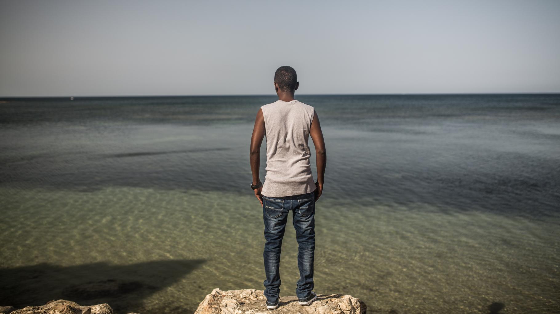 Ein Mann steht auf einem Felsen und blickt aufs Meer.