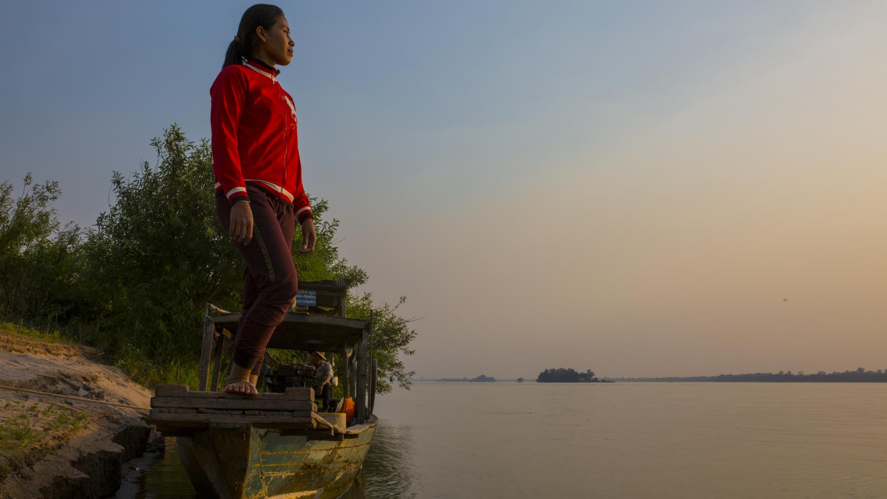 Eine Frau steht auf einem Boot und blickt über das Wasser in die Ferne