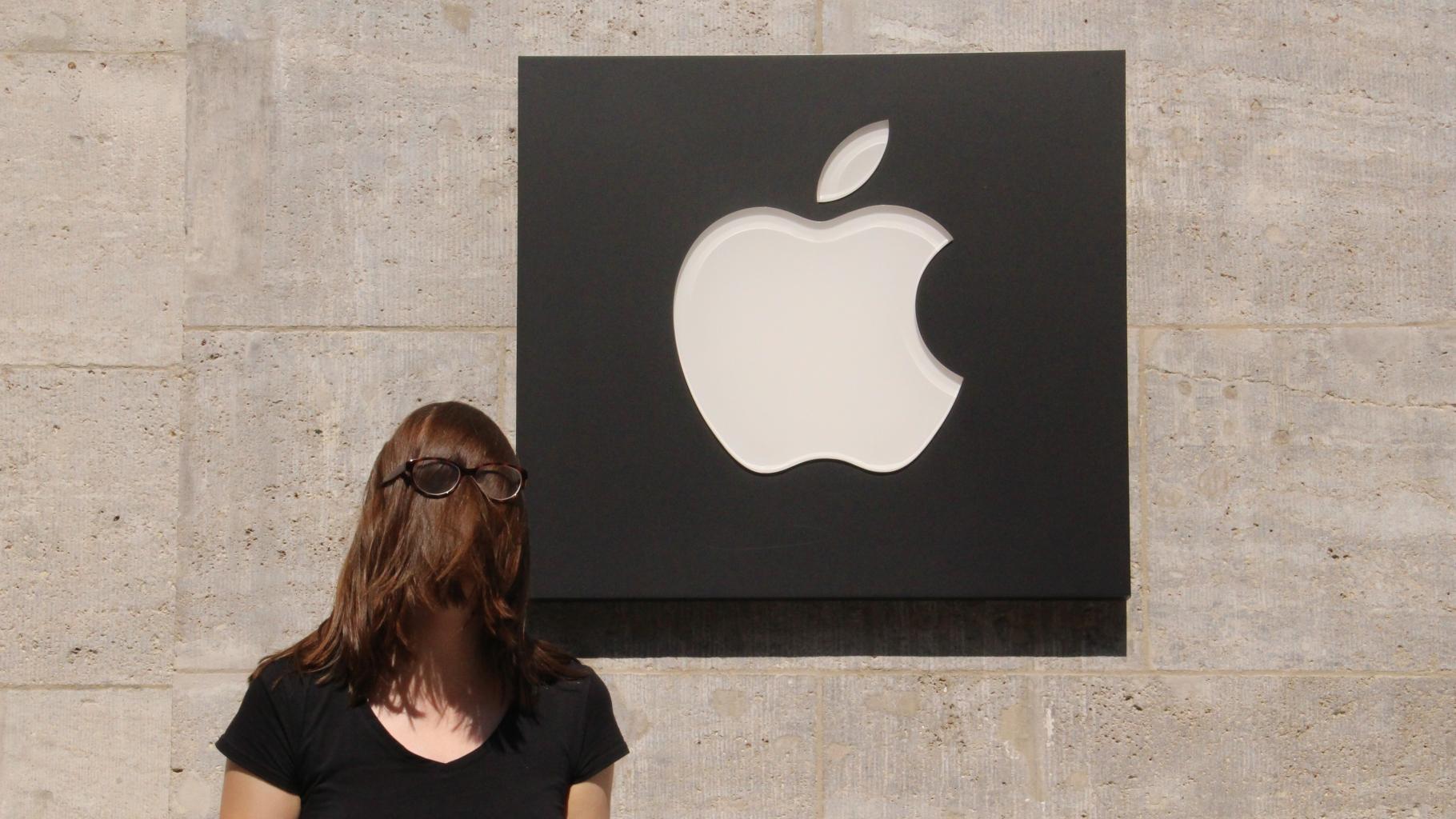 Eine Aktivistin vor einem Apple-Logo, ihr Gesicht ist durch Haare und einer darüber gezogenen Brille verdeckt