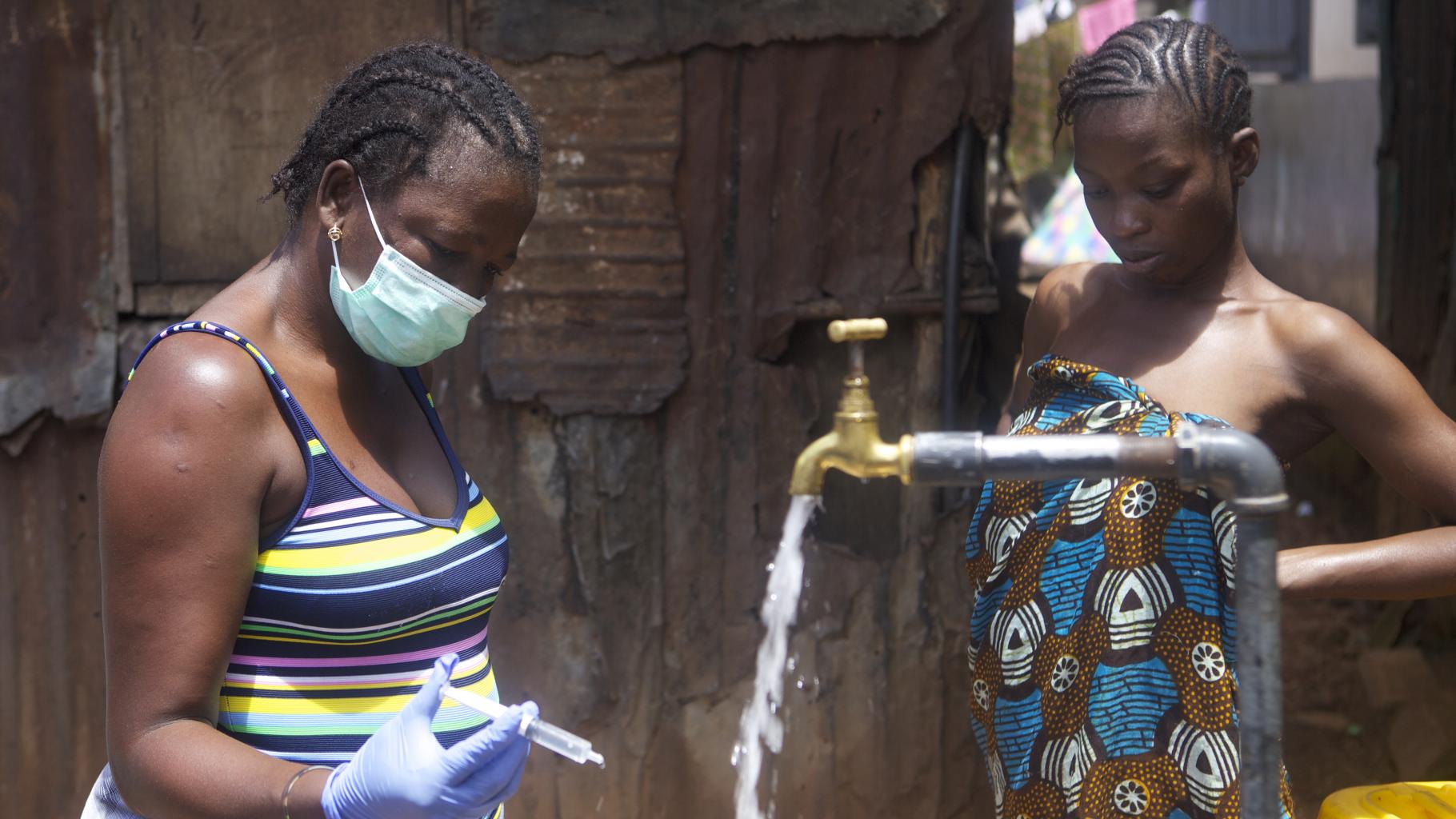 Zwei Frauen stehen an einem öffenlichen Trinkwasserhahn