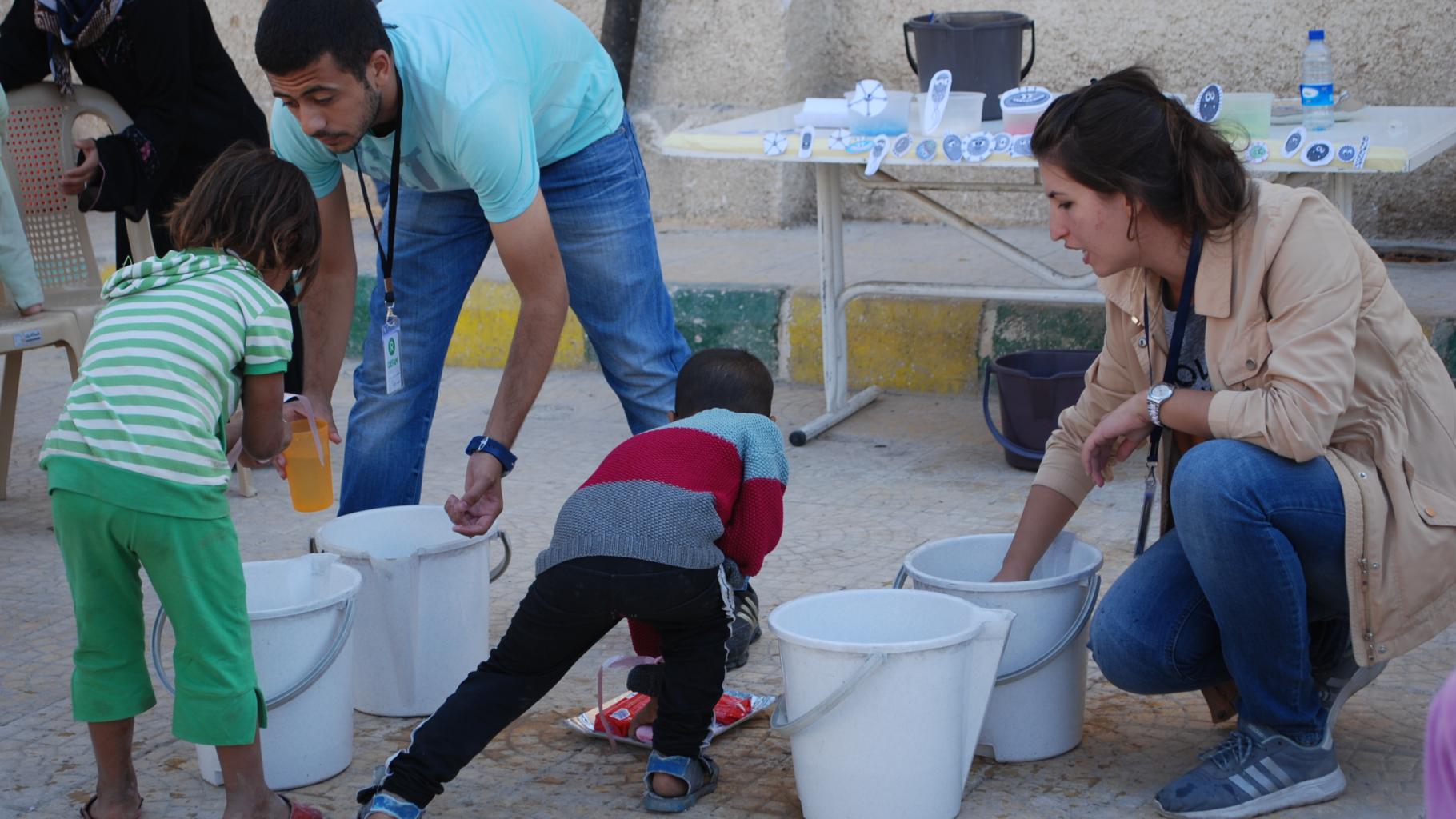 Eine Oxfam-Mitarbeiterin und ein Oxfam-Mitarbeiter erklären Kindern spielerisch die Bedeutung des Hände waschens.