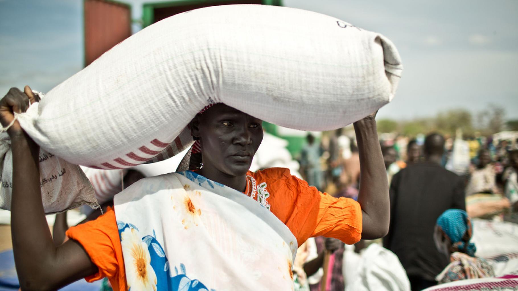 Frau aus dem Südsudan transportiert einen gefüllten Sack auf dem Kopf
