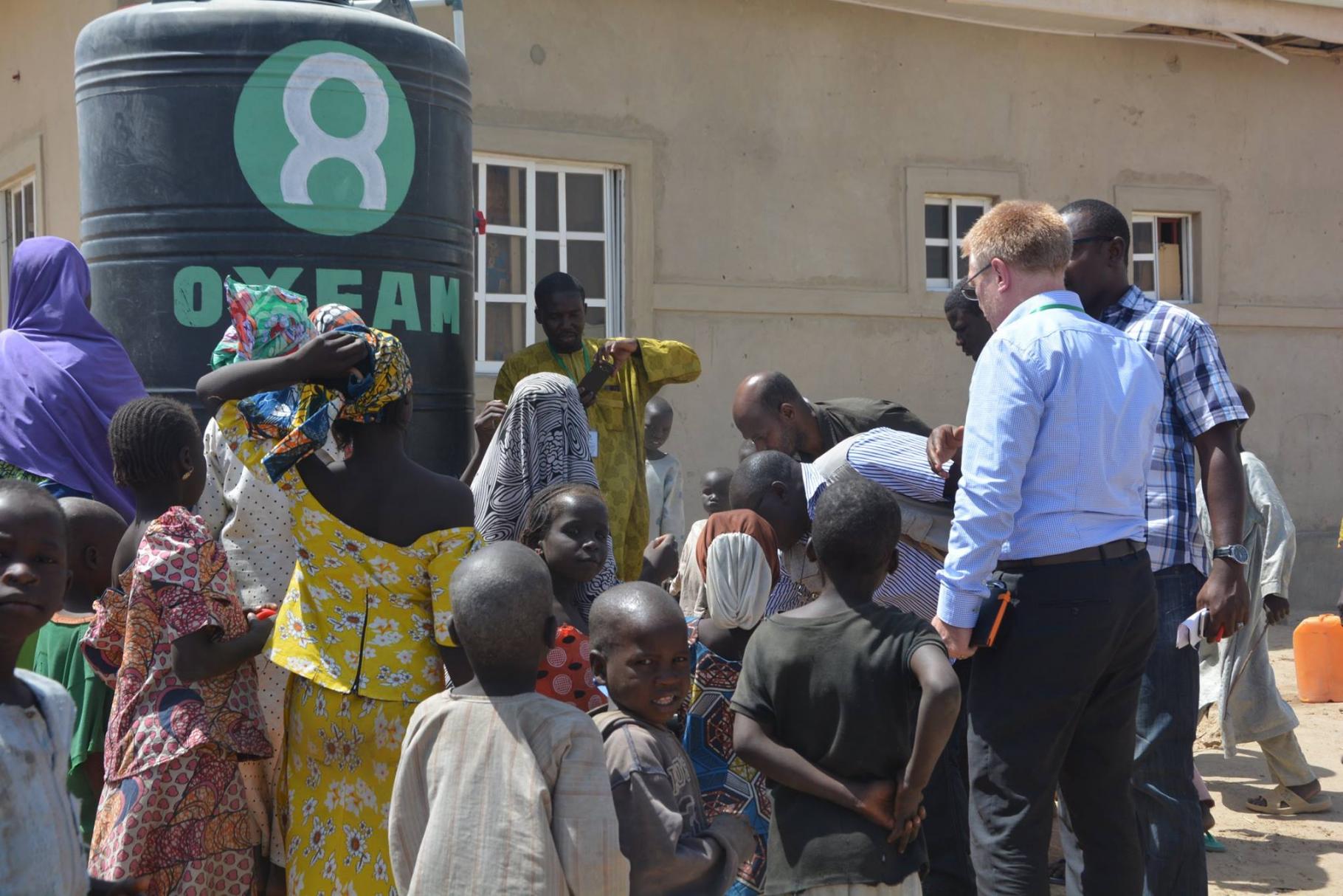 Kinder und Männer stehen um einen Oxfa-Wassertank in einem Camp für Binnenflüchtlinge, Nigeria