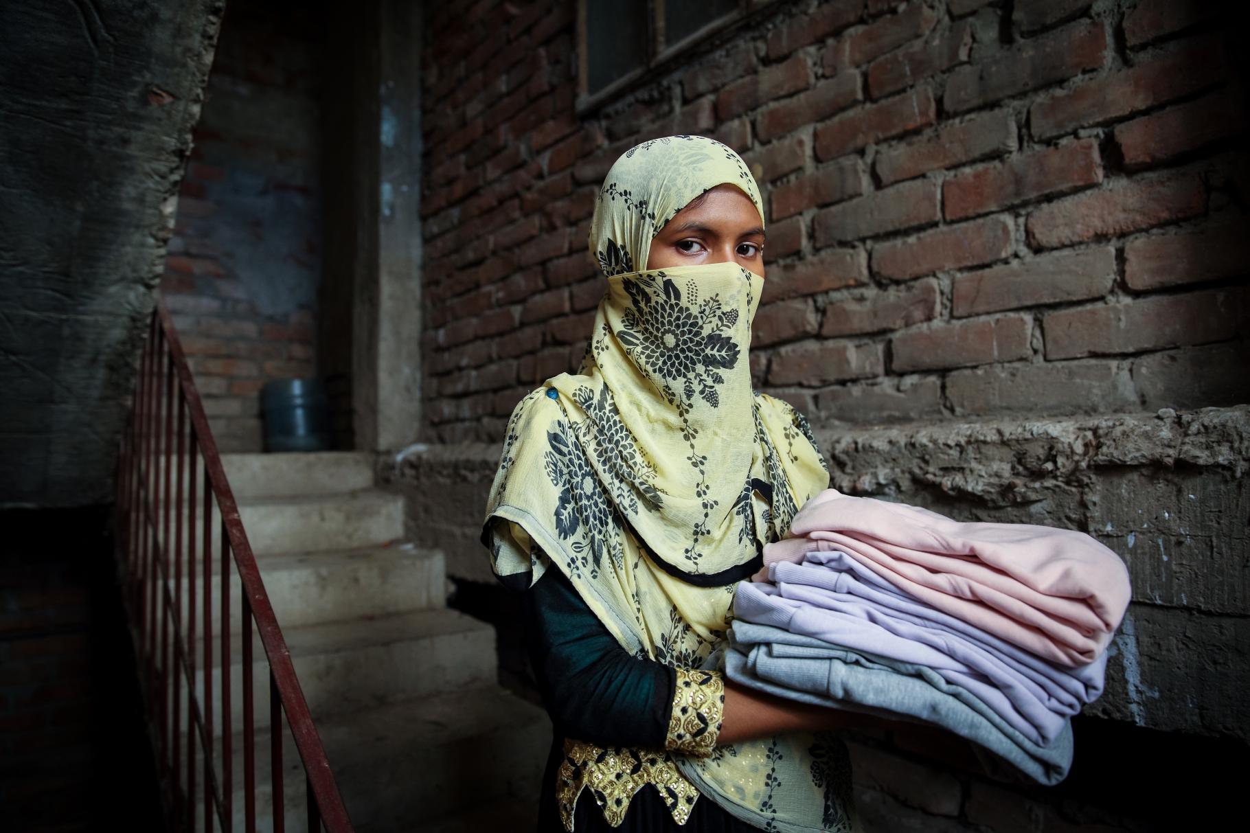 Die Textilarbeiterin Fatima hält Kleidungsstücke, die sie genäht hat.