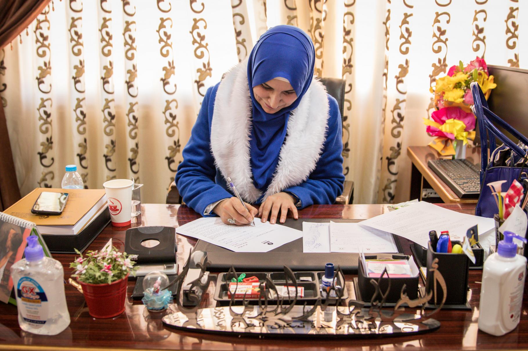 Asmaa Al Imamy sitzt an einem Schreibtisch und füllt ein Formular aus