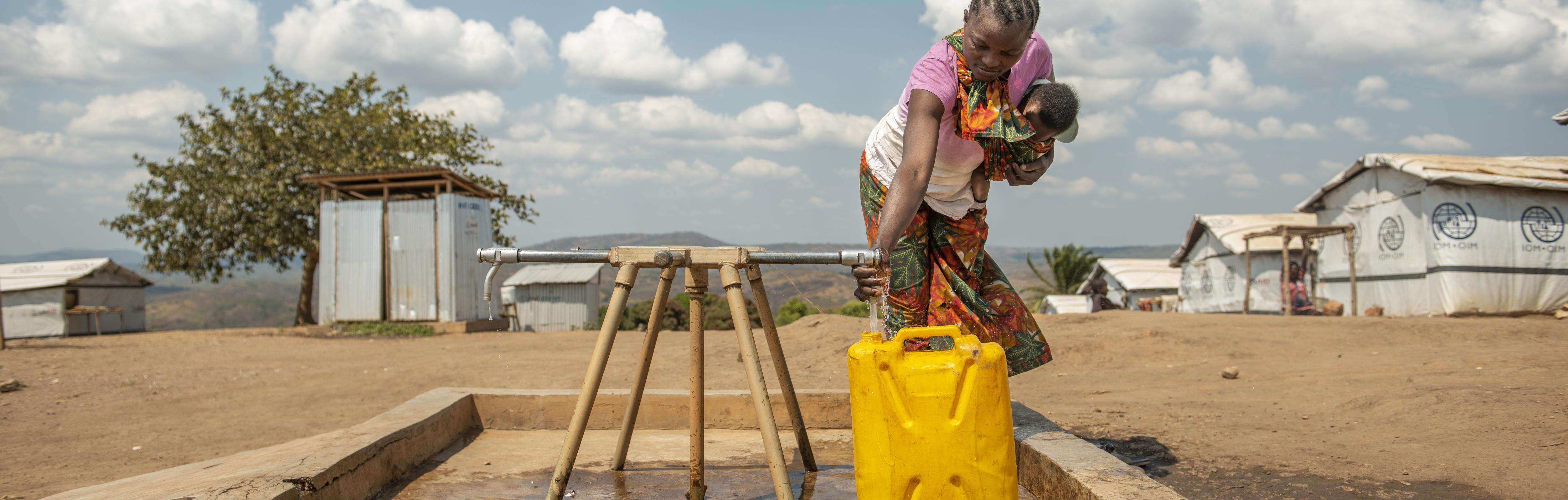 Eine Frau steht an einem Wasserhahn und befüllt einen Kanister mit Wasser.