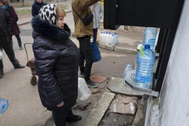 Larissisa an einer Oxfam-Wasserstelle Eine Frau steht vor einem Automaten, aus dem Wasser herauskommt und in einen Plastikkanister fließt. Mit solchen Wasserstellen, stellt Oxfam weltweit Trinkwasser zur Verfügung.