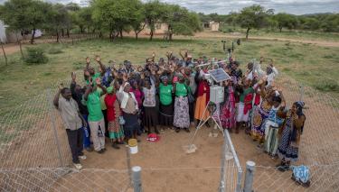 Eine Gruppe von Menschen steht bei einer Wetterstation in einer ländlichen Region in Simbabwe. Sie strecken freudig ihre Arme in die Luft.
