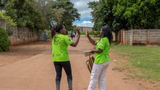 Abigail und Shylet geben sich ein High-Five auf dem Weg nachhause. Sie tragen grüne T-Shirts mit der Aufschrift "Champions-Care Work"