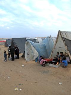 Gaza braucht Frieden Eine Szene aus einem Camp in Rafah, Gaza. Kinder bereiten essen vor einem Zelt zu. Menschen teilen Wasser aus.
