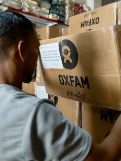Verteilung von Nahrungsmittelpaketen mit haltbaren Lebensmitteln in Nord-Gaza. Ein Mann hält einen Karton mit Oxfam-Logo. Im Hintergrund sind Regale mit Nahrungsmitteln zu sehen.