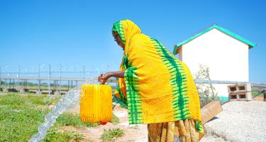 Eine Frau füllt einen gelben Wasserkanister an einer Wasserleitung.