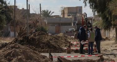 Oxfam-Kolleg*innen beraten das weitere Vorgehen zur Sanierung des Abwassersystems Drei Kolleg*innen mit Oxfam-Jacken beraten sich auf einer Straße. Um sie herum sind Bohrlöcher sichtbar, im Hintergrund ist ein Bagger zu sehen.
